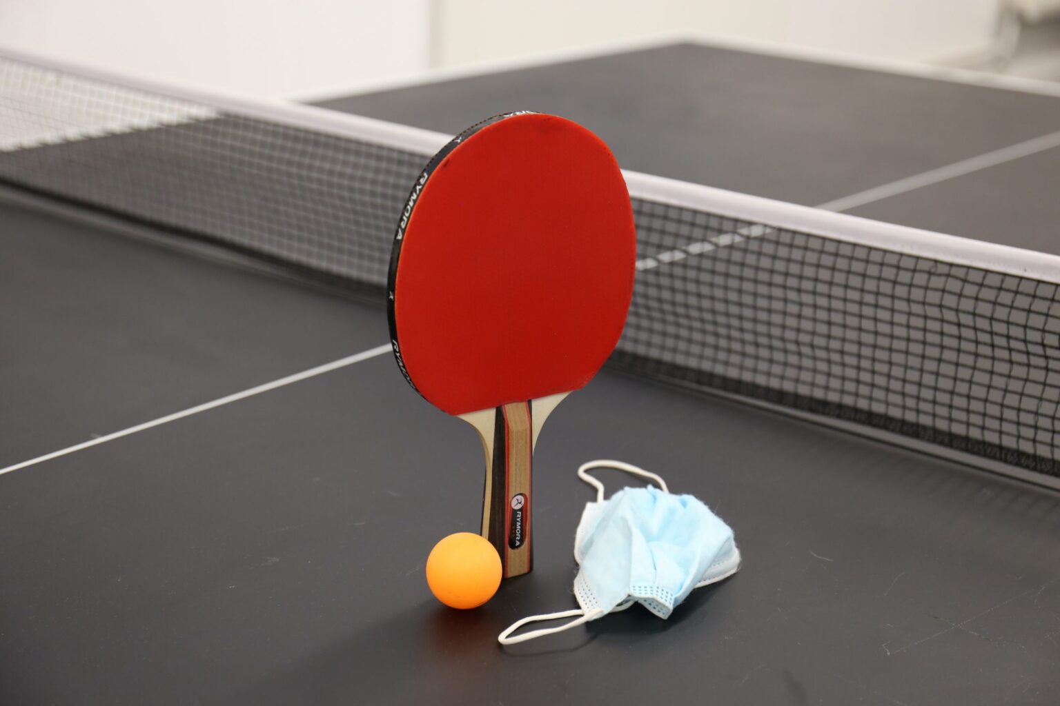 Ping pong bat and ball with face mask laid next to it